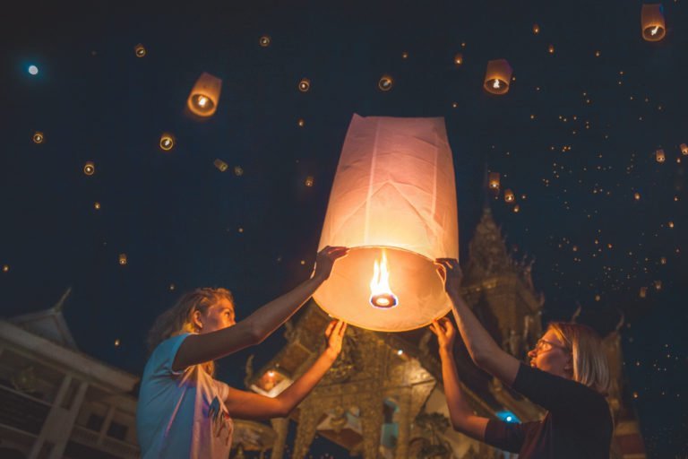 Holding a wishballoon/lantern during Chiang Mai's lantern festival Yi Peng, in front of a temple, with many lanterns lighting up the sky